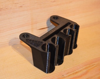 May include: A black plastic 3D printed organizer with four slots for holding items. The organizer has a textured surface and is designed to be mounted on a wall.