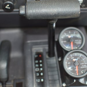 May include: Close-up of a black car interior with a gear shifter and two round gauges. The gauges are labeled "Boost" and "Fuel Pressure".