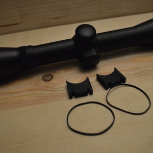 May include: A black rifle scope with a 1-4x32 magnification, two black scope rings, and two black rubber bands.