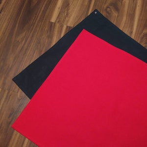 May include: Two fabric backdrops, one red and one black, are laid out on a wooden floor. The red backdrop is on top of the black backdrop.