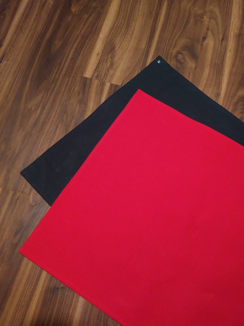 May include: Two fabric backdrops, one red and one black, are laid out on a wooden floor. The red backdrop is on top of the black backdrop.