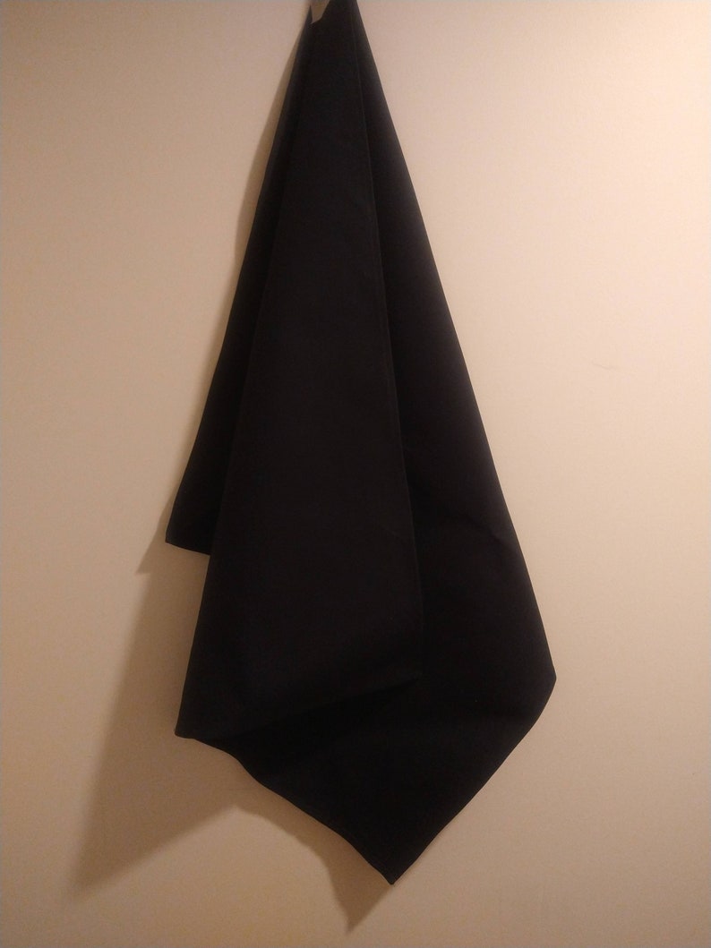 May include: A black fabric hanging on a wall. The fabric is folded in half and is hanging from a hook.