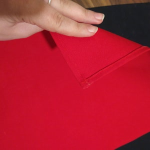 May include: A red fabric tablecloth with a folded edge. The tablecloth is on a black surface.