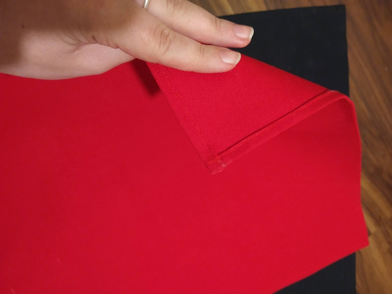 May include: A red fabric tablecloth with a folded edge. The tablecloth is on a black surface.