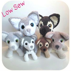 May include: A collection of handmade crochet dog plushies in various sizes and colors. The dogs feature large, expressive eyes and are primarily gray, brown, and white. The text "Low Sew" is written in pink cursive in the upper left corner.