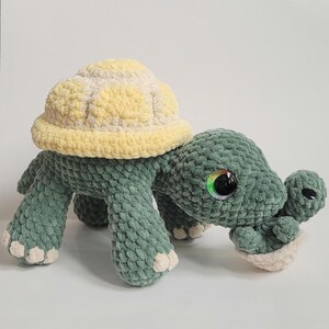 May include: A handmade crochet turtle plush toy in shades of green and yellow. The turtle has a textured shell, large, colorful eyes, and a smaller baby turtle. The plush is soft and cuddly, perfect for children or as a decorative item.
