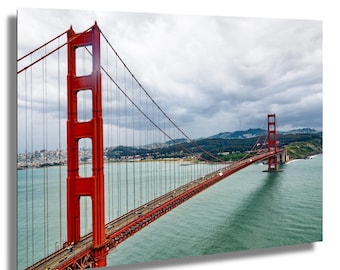 May include: A vibrant image of the Golden Gate Bridge in San Francisco, California. The iconic red bridge spans across the water under a cloudy sky. Cars are visible on the bridge, and the surrounding landscape includes hills and the city skyline.