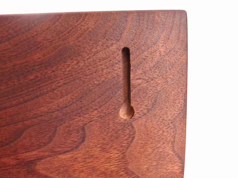 May include: Close-up of a wooden plaque with a dark brown finish. The wood grain is visible. A vertical keyhole slot is carved into the wood, with a circular opening at the bottom. The plaque is likely for wall mounting.
