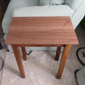 May include: A small, square wooden side table with a rich brown finish. The table has a simple design with four angled legs. The tabletop measures approximately 20 inches by 20 inches.