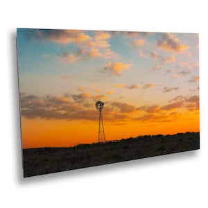 May include: A scenic landscape photograph featuring a windmill silhouetted against a vibrant sunset. The sky transitions from orange to blue, with fluffy clouds. The windmill stands on a grassy hill.