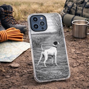 Op de afbeelding: Transparante telefoonhoes met een zwart-wit afbeelding van een Pointer-hond op een pad. De hoes is omgeven door outdoorkleding, waaronder wandelschoenen, een kaart en een rugzak. De hond heeft een zwarte kop en een wit lichaam.