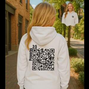 May include: Cream-coloured hoodie with a hood and long sleeves. The back features a large black QR code with the text "Proverbs 3:5" printed in black. A smaller image of a person wearing a similar hoodie is in the upper right corner.