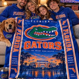 May include: A blue fleece blanket featuring the Florida Gators logo, the text "FLORIDA GATORS THE SWAMP RUNS DEEPER", an illustration of Ben Hill Griffin Stadium at sunset, and the text "GAINESVILLE, FL EST. 1853" with orange and white vertical stripes.