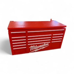 Pu&ograve; includere: Cassetta degli attrezzi rossa con strisce orizzontali bianche e logo Milwaukee in bianco. La cassetta ha una forma rettangolare con coperchio incernierato e pi&ugrave; cassetti. Progettata per riporre gli attrezzi.