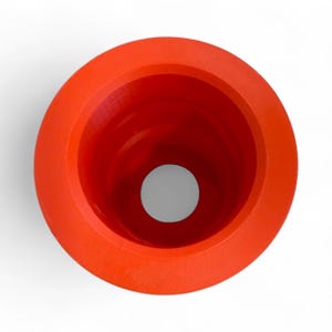 May include: A bright orange, funnel-shaped object with a wide, circular rim and a small, central opening. The interior is a deep red, and the exterior has a textured surface. The object is set against a white background.