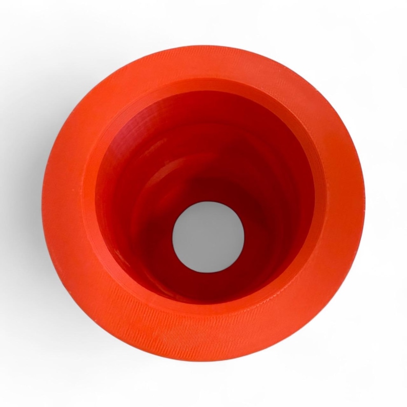 May include: A bright orange, funnel-shaped object with a wide, circular rim and a small, central opening. The interior is a deep red, and the exterior has a textured surface. The object is set against a white background.