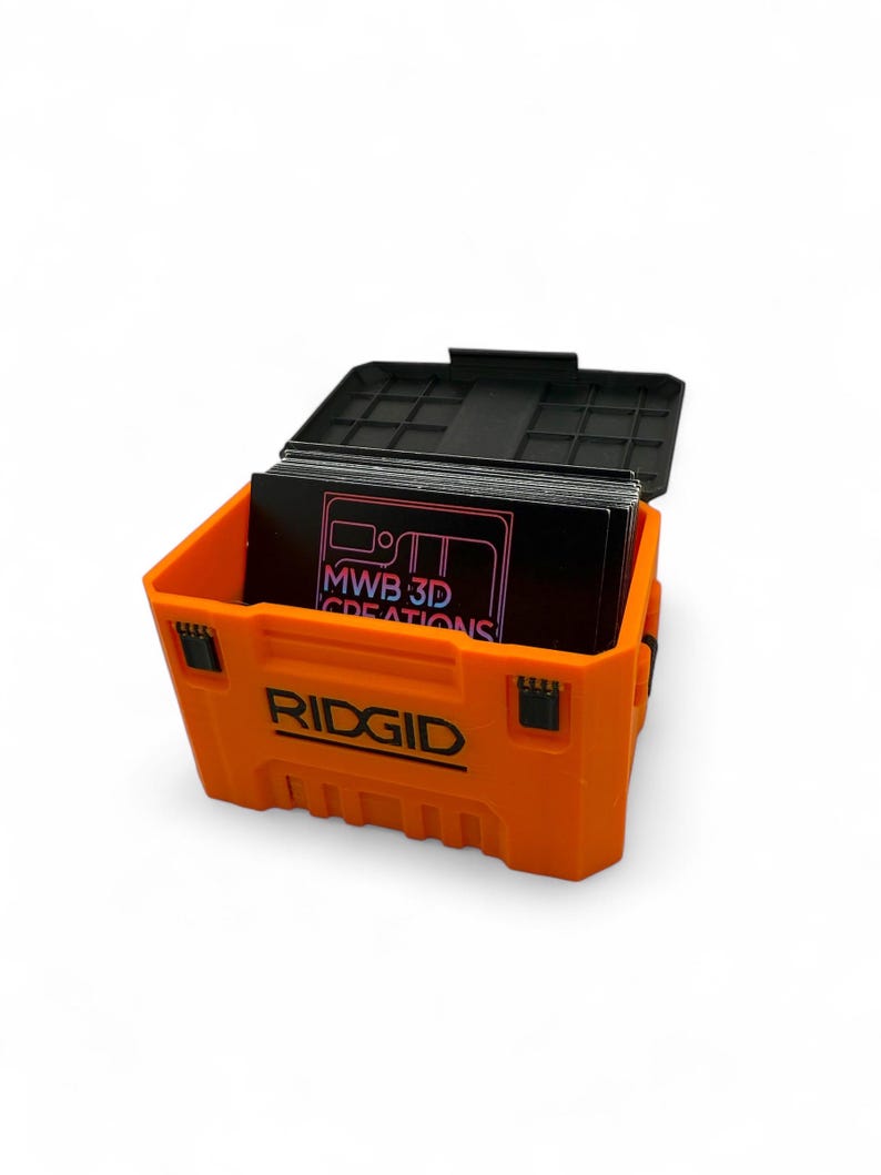 May include: An orange plastic tool box with the word "RIDGID" printed on the front. The box is open and contains a stack of black business cards with the text "MWB 3D CREATIONS" printed on them.