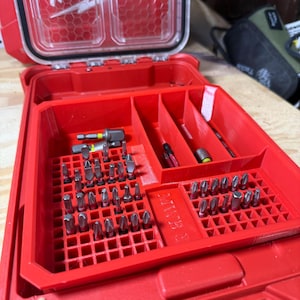 May include: Red tool organiser with a clear lid, filled with various metal drill bits. The organiser has multiple compartments for organisation. The Milwaukee logo is visible on the side.
