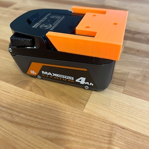 Puede incluir: Un soporte de bater&iacute;a impreso en 3D de color naranja para una bater&iacute;a de iones de litio negra de 18 V con una capacidad de 4 Ah. La bater&iacute;a tiene el texto "MAX OUTPUT LITHIUM" impreso en ella.