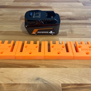 Puede incluir: Cuatro soportes de bater&iacute;a de pl&aacute;stico naranja con el texto "MWB" impreso en cada uno. Los soportes est&aacute;n dise&ntilde;ados para contener una bater&iacute;a de litio MAXPOWER 18V 4Ah negra y naranja.