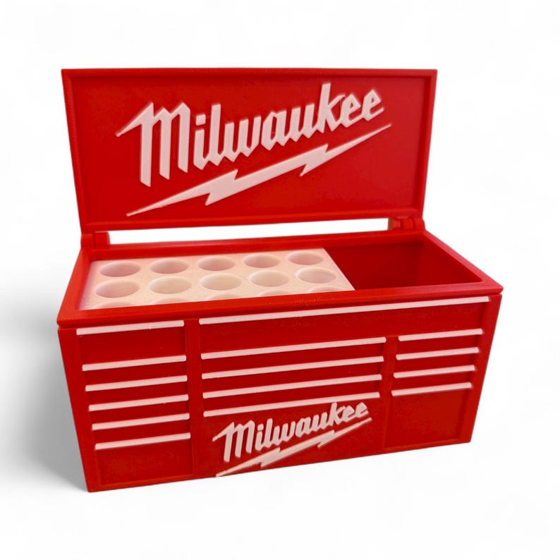 Pu&ograve; includere: Un cassetta degli attrezzi rossa con il logo Milwaukee bianco sul coperchio e sulla parte anteriore. La cassetta ha strisce orizzontali bianche e un vassoio interno bianco con pi&ugrave; aperture circolari.