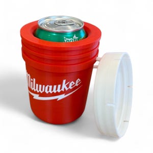 May include: A red plastic can cooler with the word "Milwaukee" in white. A green can of Sprite is inside the cooler. A white handle is attached to the side of the cooler.