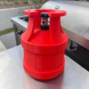 May include: A bright red propane tank with a black valve and a silver metal surface in the background. The tank has a cylindrical shape with a rounded top and bottom. The tank has a series of decorative geometric shapes around the middle.
