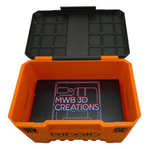 May include: An orange plastic storage box with a black lid. The lid has a grid of compartments. The box is open and has a black foam insert with the text "MWB 3D CREATIONS" printed on it. The box is labeled "RIDGID".