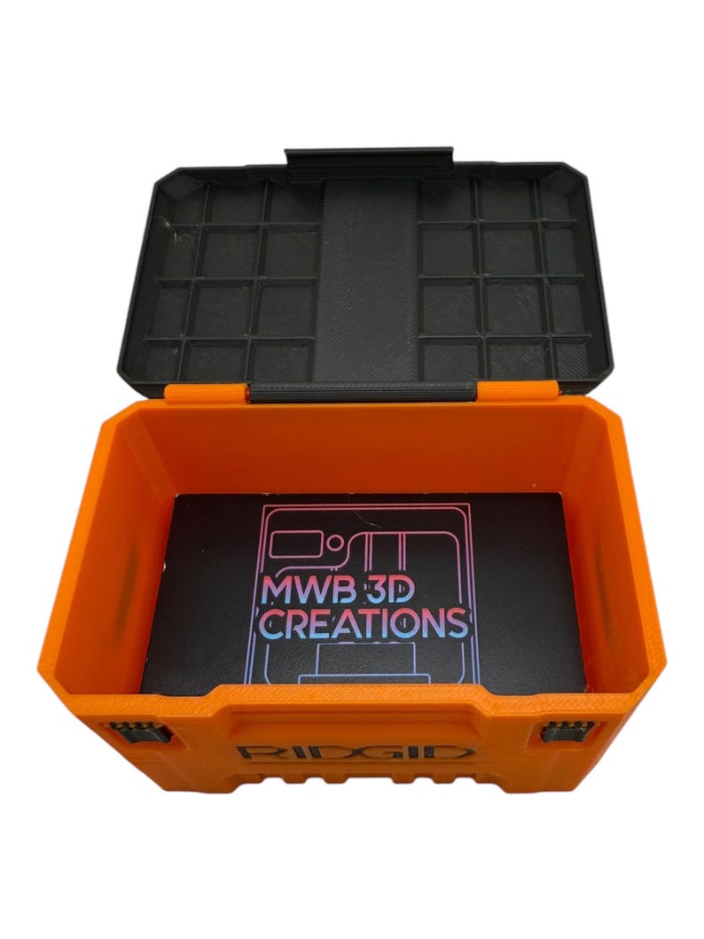 May include: An orange plastic storage box with a black lid. The lid has a grid of compartments. The box is open and has a black foam insert with the text "MWB 3D CREATIONS" printed on it. The box is labeled "RIDGID".