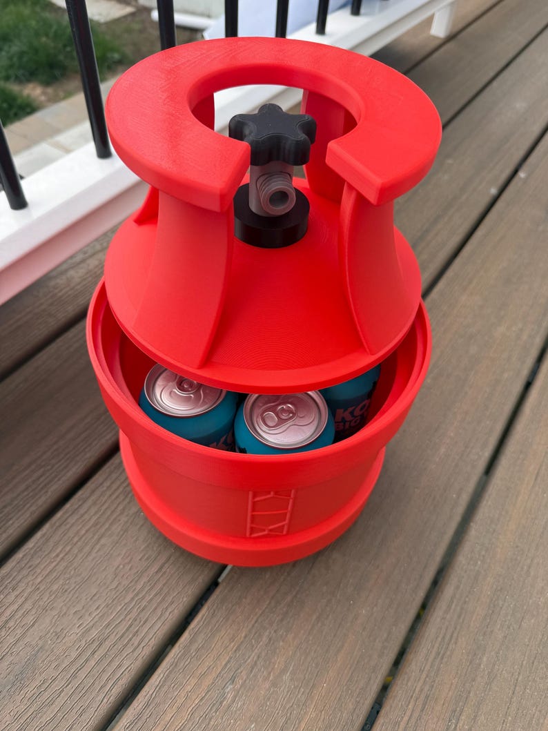 May include: A red, cylindrical cooler with a black valve and star-shaped handle. The cooler holds several blue cans. The cooler has a unique design and is sitting on a wooden deck.
