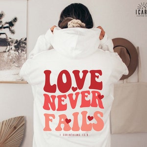 a woman wearing a white hoodie with the words love never falls printed on it