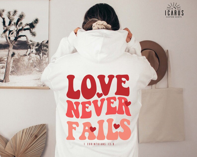 a woman wearing a white hoodie with the words love never falls printed on it
