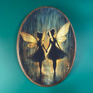 May include: Oval-shaped artwork featuring two silhouetted figures of fairies holding hands. The fairies have golden wings and are set against a backdrop of blue and gold hues. The artwork is framed with a brown border.