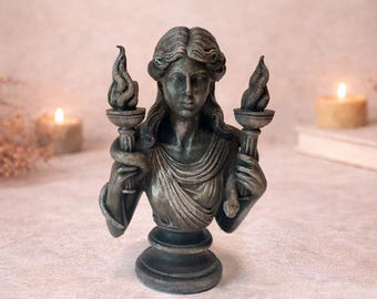 May include: A detailed bust of a woman with flowing hair, holding two torches with flames. The statue is a muted silver color and has a decorative base. The bust is a classical sculpture.