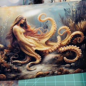 May include: A rectangular art print featuring a fantasy illustration of a figure with long flowing hair and a golden octopus lower body, positioned amidst an underwater scene with coral, rocks, and aquatic plants in shades of gold and blue.