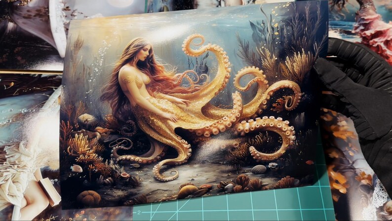 May include: A rectangular art print featuring a fantasy illustration of a figure with long flowing hair and a golden octopus lower body, positioned amidst an underwater scene with coral, rocks, and aquatic plants in shades of gold and blue.