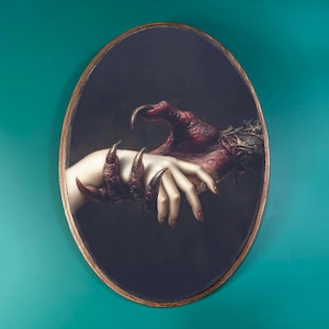 May include: Oval-shaped artwork depicting a human hand clasped by a clawed, red hand. The artwork has a dark background and a gold-colored frame. The clawed hand appears to be reaching out to grasp the human hand.
