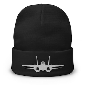 May include: Black beanie with a white embroidered jet fighter design on the folded brim. The beanie is made of a soft, knitted material. The design is a detailed outline of the aircraft.