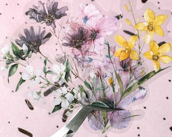Può includere: Un foglio di adesivi trasparente con un design a bouquet floreale. Il bouquet comprende fiori viola, rosa, bianchi e gialli con foglie verdi. Una pinzetta argentata è posizionata nella parte inferiore.