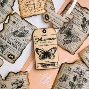 May include: A collection of vintage-style paper ephemera with butterfly and text designs. The pieces include tags and cut-out shapes with aged edges, printed with French phrases and botanical illustrations.