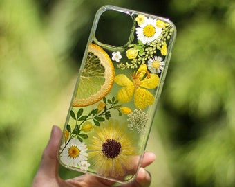 May include: A clear phone case with pressed flowers and a slice of dried citrus fruit. The flowers are yellow, white, and green. The citrus fruit is orange.
