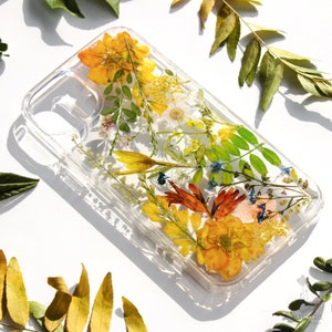 May include: A clear phone case with pressed flowers and leaves. The flowers are yellow, orange, and red. The leaves are green.