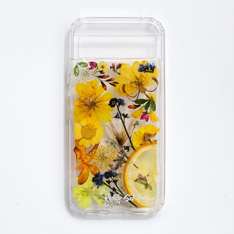 May include: A clear phone case with a pressed flower design. The case features yellow, orange, and white flowers, as well as a slice of lemon. The text "Ready Set Grow" is printed on the case.