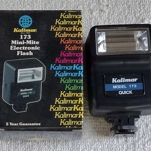 Può includere: Un flash elettronico Kalimar modello 173 Mini-Mite nero con una garanzia di 5 anni. Il flash è nella sua confezione originale, che presenta il logo Kalimar e il testo "Mini-Mite Electronic Flash".