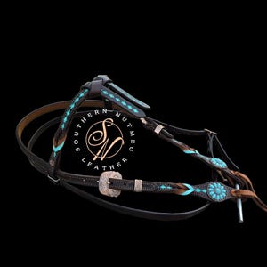 May include: A dark brown leather horse bridle featuring turquoise inlay accents, braided leather details, and silver-toned metal hardware. The piece includes decorative floral-shaped turquoise conchos and a buckle, with the text Southern Nutmeg Leather.