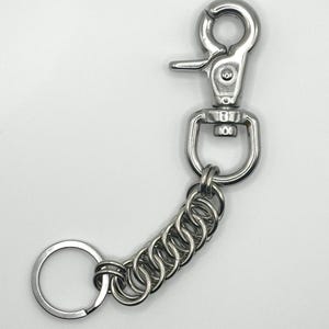 Könnte beinhalten: Ein silberner Schlüsselanhänger mit einem großen, federbelasteten Verschluss und einem runden Schlüsselring. Die Kette besteht aus mehreren ineinandergreifenden Metallringen.