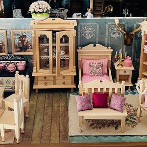 Könnte beinhalten: Miniatur-Puppenhaus-Interieur mit Schlafzimmer, Essbereich und Wohnzimmer. Das Set umfasst helle Holzmöbel wie Bett, Bank, Tisch und Schränke. Die Dekoration weist rosa und weiße Akzente auf.