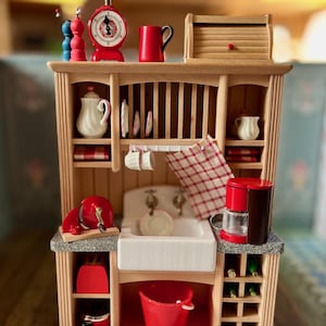 Könnte beinhalten: Ein Miniatur-Küchenspielset aus Holz in Rot und Weiß. Das Set enthält eine Spüle, eine Kaffeemaschine, eine Waage, einen Geschirrständer und Regale.
