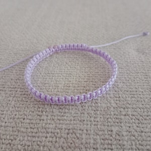 May include: A light purple braided bracelet with a simple design.