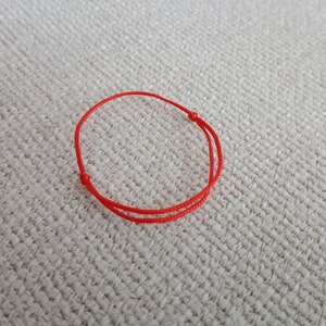 May include: A red string bracelet with a simple knot design.